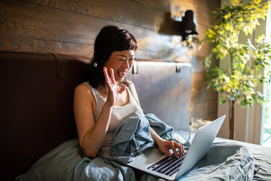 Smiling woman video chatting from bed at home