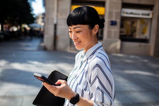 Smiling businesswoman using smartphone on city street