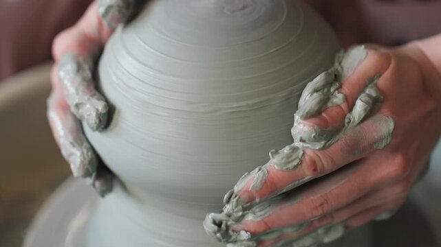 Pottery clay shaping. Ceramic artist molding vessel. Wheelthrowing session with apprentice smoothing clay surface. Artisan focuses on centering and shaping wet clay during pottery lesson