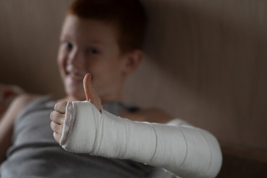 Portrait of a teenager happily raising his thumb up with his arm in a plaster cast and smiling