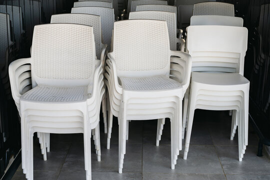 White plastic chairs stacked outdoors at a restaurant or resort, empty seating arrangement with repetitive pattern and modern Mediterranean summer atmosphere