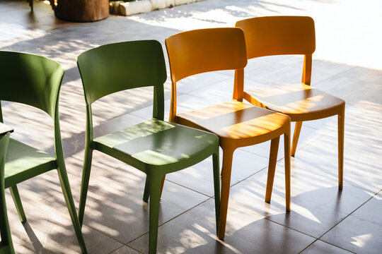 Colorful green and orange chairs in outdoor seating area, sunny summer resort setting with geometric shadows on tiled floor