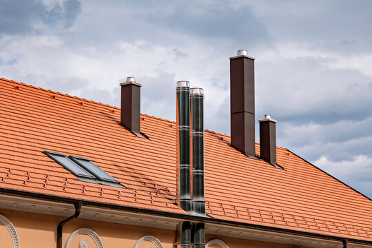 Residential building roof featuring various chimneys and skylights under a cloudy sky, showcasing contemporary architecture and construction elements