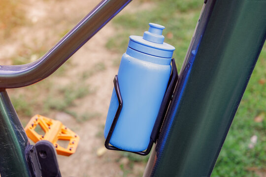 Blue water bottle fixed in a cage on a bicycle frame, promoting hydration during outdoor cycling activities and sports