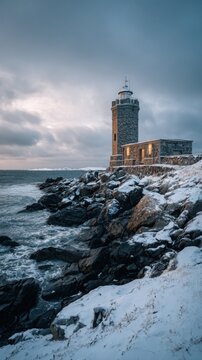 Ultra realistic professional coastal winter photography of an old lighthouse standing beside a frozen rocky coastline, snow covered ground, dark