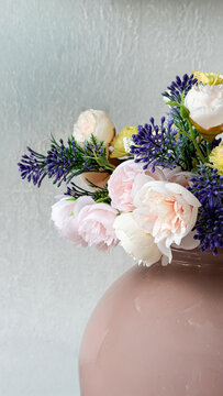 Elegant pastel artificial flower arrangement in a glossy pink vase against a neutral textured wall, decorative floral interior composition with copy space.