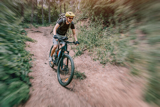 Young man enjoying mountain biking adventure, wearing helmet and backpack, cycling downhill fast on a dusty forest path