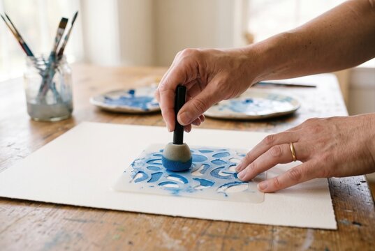 Person using a sponge dabber to apply blue paint over a plastic stencil on paper