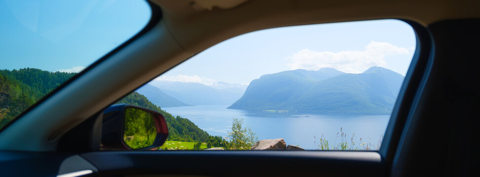 Side window view from a moving car showing a fjord and high mountains in Norway. Wide angle view. Natural scenic landscape during a road trip.