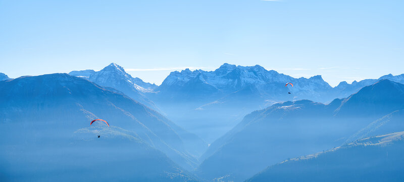 Paragliders flying in sky against mountain range layers on sunny day. Outdoor extreme sport, recreation and mountain view concept.