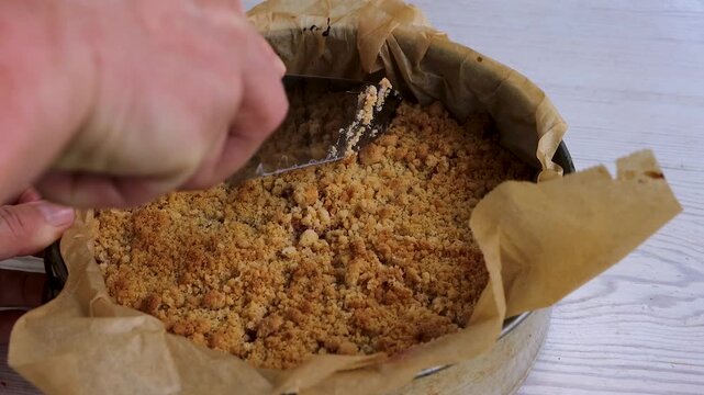 Hands cutting homemade crumb cake with a kitchen knife in a parchment-lined springform pan.