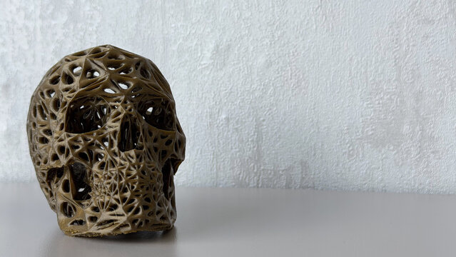 Abstract decorative skull sculpture with intricate openwork structure on a neutral textured background, modern artistic home decor with copy space.
