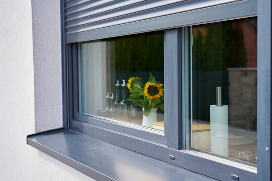 Roller shutter is partly lowered over kitchen window with sunflowers and paper towel visible inside