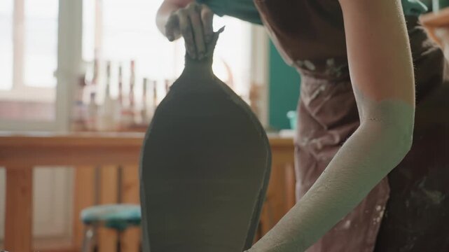 White female ceramist trimming vase rim precisely on wheel in bright workshop, closeup of hands and tool smoothing silhouette, focused finishing and control, tactile studio atmosphere