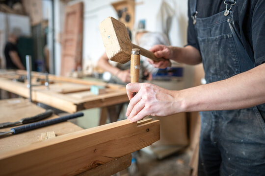Hardworking carpenter in restoration workshop renovating wooden frame with mallet and chisel tools, professional master in repair shop applying knowledge, professional skills, developing craftsmanship