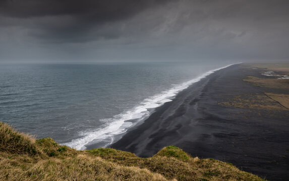 Reynisfjara black sand beach from Dyrholaey Peninsula viewpoint. Coastal landscape black volcanic sand beach atlantic ocean waves moody sky Iceland icelandic landscape