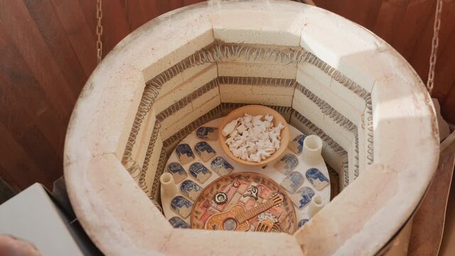 White potter opening kiln to inspect bisque pieces on shelf, overhead view of cooled ceramics careful hands reach in with heatproof gloves, soft studio light, calm anticipation, bowls and plates