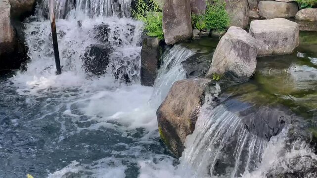 Clear fresh water cascades over smooth rocks into a peaceful pond, creating foaming splashes and gentle ripples
