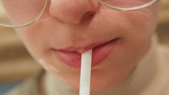 Frontal lips glasses straw sip portrait, stylish person sipping through paper straw with rimmed glasses and turtleneck, cafe backdrop and glossy lip texture, relaxed urban lifestyle tone and candid