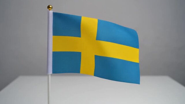 Small Sweden Flag Waving on White Table Desk Stand Isolated on Grey Background