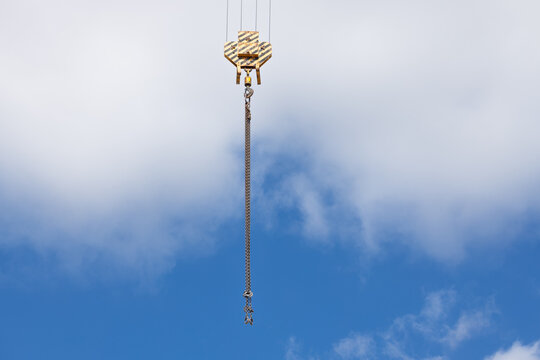 Construction crane hook with chain suspended against a clear blue sky, showcasing industrial equipment used in building and heavy lifting operations