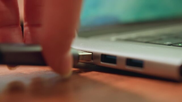 Student working with technology setup. White hands insert gadget into laptop while glowing LED indicates activity. Person connecting peripheral to laptop on cozy desk during evening study session