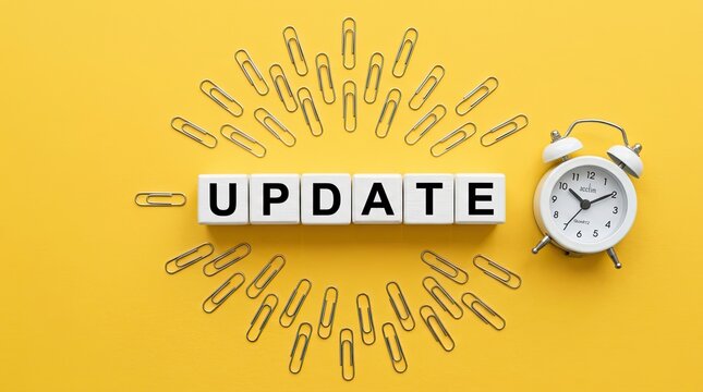 Modern update concept with white blocks spelling 'update' and alarm clock on yellow background with symbolizing time sensitive changes blocks surrounded paper depicts word update update spelled