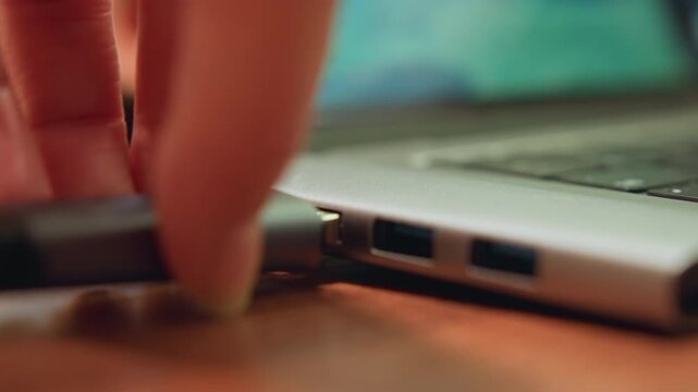 Closeup laptop usb port hand inserting flash drive on wooden desk, warm evening light, focused freelancer backing up important files to external storage, slow deliberate motion, shallow depth