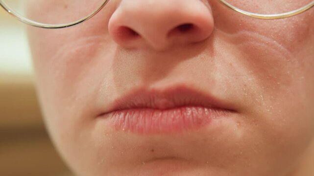 Closeup caucasian woman listener pensive silence, lips pressed and unsmiling with glasses rim, subtle tension in jaw and skin pores visible, quiet contemplative mood for interview or reflective