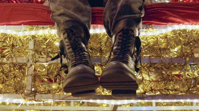 Boots tapping beneath holiday lights, lowangle shot of musician keeping tempo on bench with scuffed leather boots and shimmering tinsel backdrop, energetic urban vibe and candid nighttime atmosphere