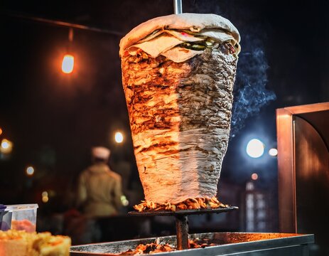 delicious shawarma cooking on rotating spit over hot coals at a street food vendor stall at night time