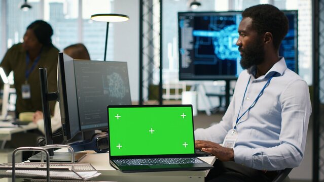 Startup office programmer develops artificial intelligence models for business analytics on a green screen laptop, running forecasting simulations with a replaceable mockup notebook.
