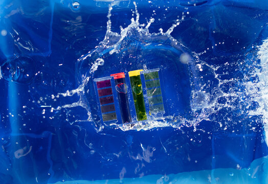 PH acid level test kit on quality water on purple yellow. PH acid level tester kit fall on water splashing splattering over blue background, top angle