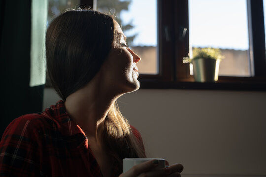 Woman enjoying morning sunlight with coffee at home
