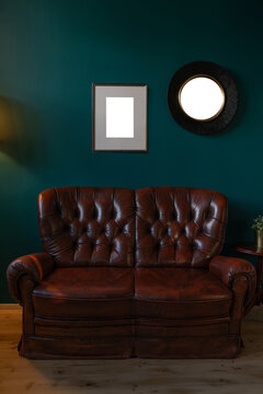 Vintage leather sofa with blank frame and mirror on teal wall