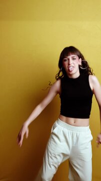 Cheerful young woman dancing and smiling against yellow background