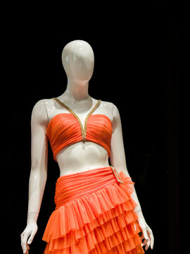Female Mannequin Wearing Orange Two Piece Ruffled Dress on Black Background