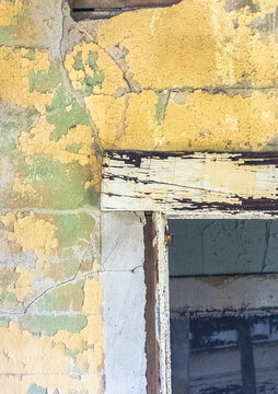 Cracked, broken and peeling yellow paint around a doorframe inside an old rundown and abandoned house.