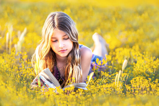 Young girl reading a book outdoors in a field of yellow wildflowers