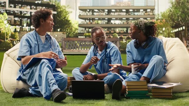 The diverse group of medical students collaborates with a laptop on campus, combining discussion, peer tutoring and outdoor group study for medical school training and science education.