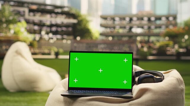 The laptop displays a green screen mockup on a modern campus beanbag, offering an editable display for education and digital learning against an empty campus backdrop with blank-screen replacement.