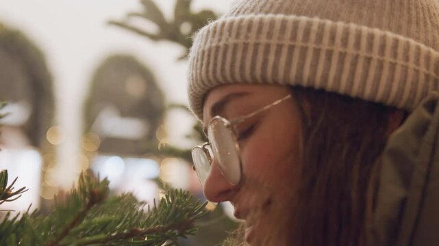 Joyful observer among festive lights. Calm artist enjoys illuminated seasonal market scene. Artistic person with round spectacles marvels at illuminated tree branches in cheerful market setting