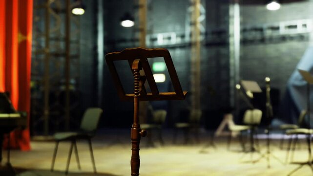 Closeup music stand on dim stage, shallow depth with bokeh chairs and piano edge, red curtain hint and focused brass stand detail, intimate solo practice vibe