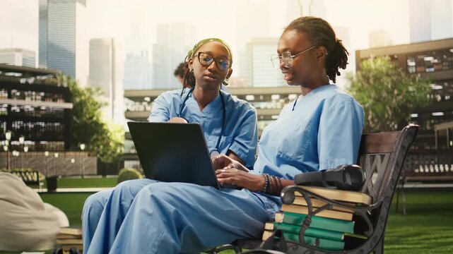 Medical students exchange ideas with a laptop and notes during outdoor group study on a campus bench, combining medical training and peer tutoring.