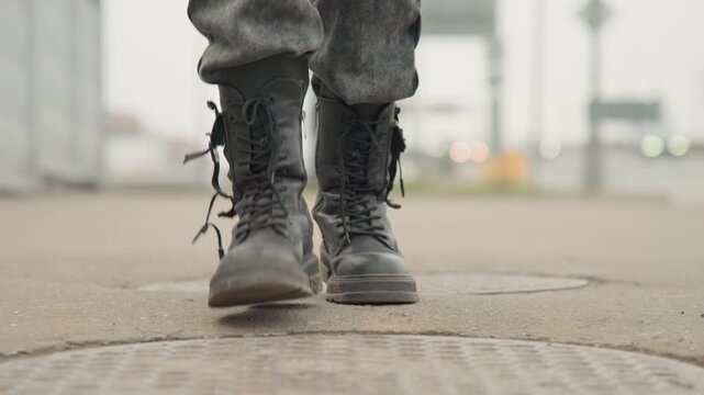 Boots stepping on manhole cover in street, lowangle closeup showing scuffed leather, laces and purposeful pace, muted urban background, gritty determined motion ideal for journey or military themes