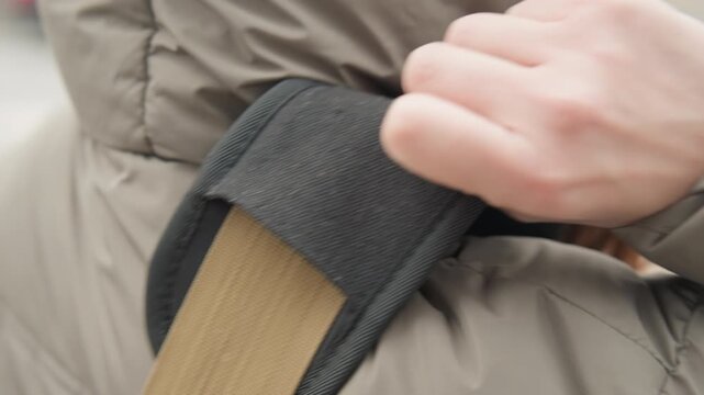 Closeup white student fastening backpack strap with fingers, visible padding and stitching on puffer coat, hooded winter jacket, focused preparatory gesture before heading to class