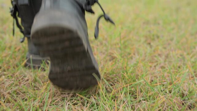 Black leather boots walking on grass close up low angle shots of rugged tactical boots stepping through damp field, laces untied and scuffed soles leaving faint prints in earth slow steady pace evokes