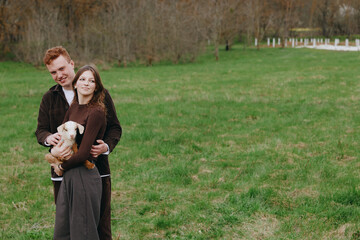 Obraz premium Smiling couple outdoors with a goat kid in a grassy field, embracing warmly. A lifestyle moment displaying family bonding, rural living, and animal companionship in natural light.