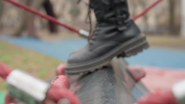 Boots striding curved pipe with attitude, confident punk performer balancing on textured tube secured by red rope anchors, bold scuffed leather and heavy sole hitting surface, urban alley backdrop