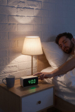 man lying in bed reaching arm to turn off green digital alarm clock showing 400 on bedside